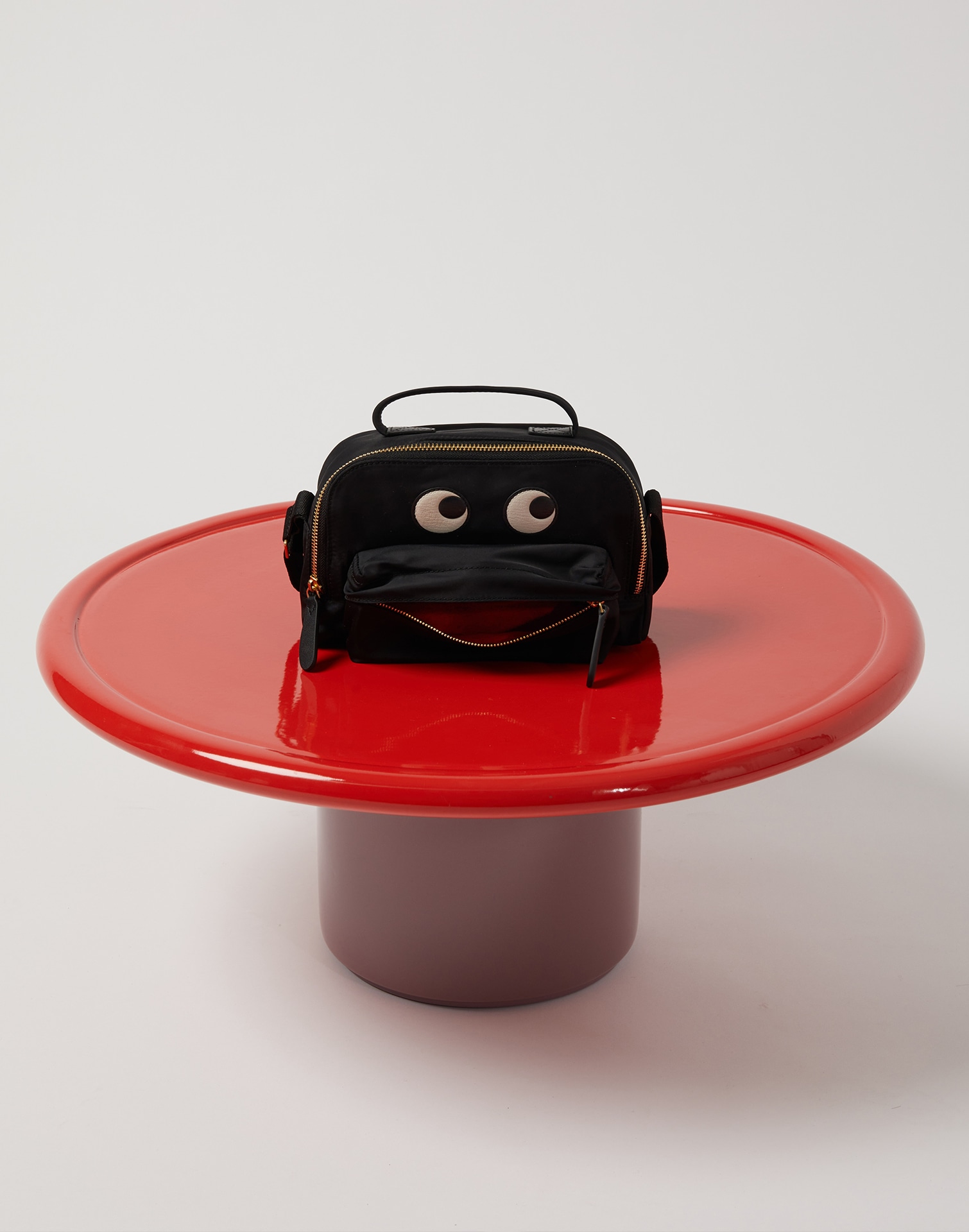 Black handle bag from Anya Hindmarch sitting on a red table