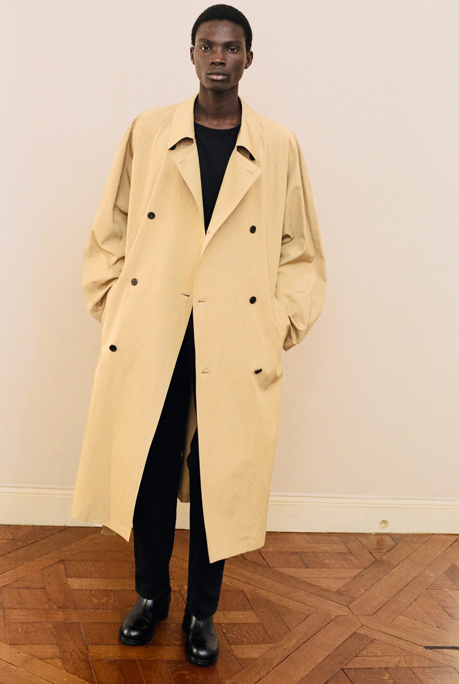 The Row整体造型：模特身穿一件长款卡其色大衣，搭配纯黑色造型和黑色皮靴。