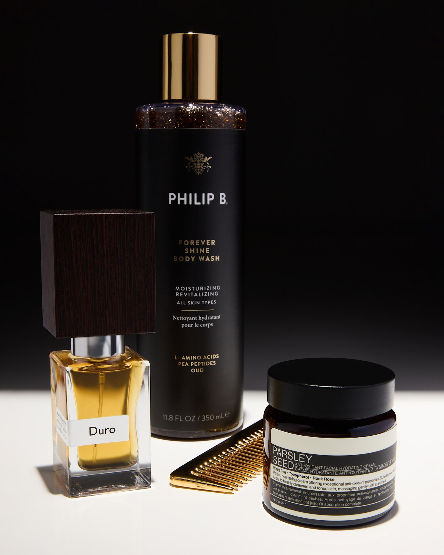 Small Duro perfume bottle, Phillip B. body wash, gold comb and jar of parlsey seed cream against black and white background