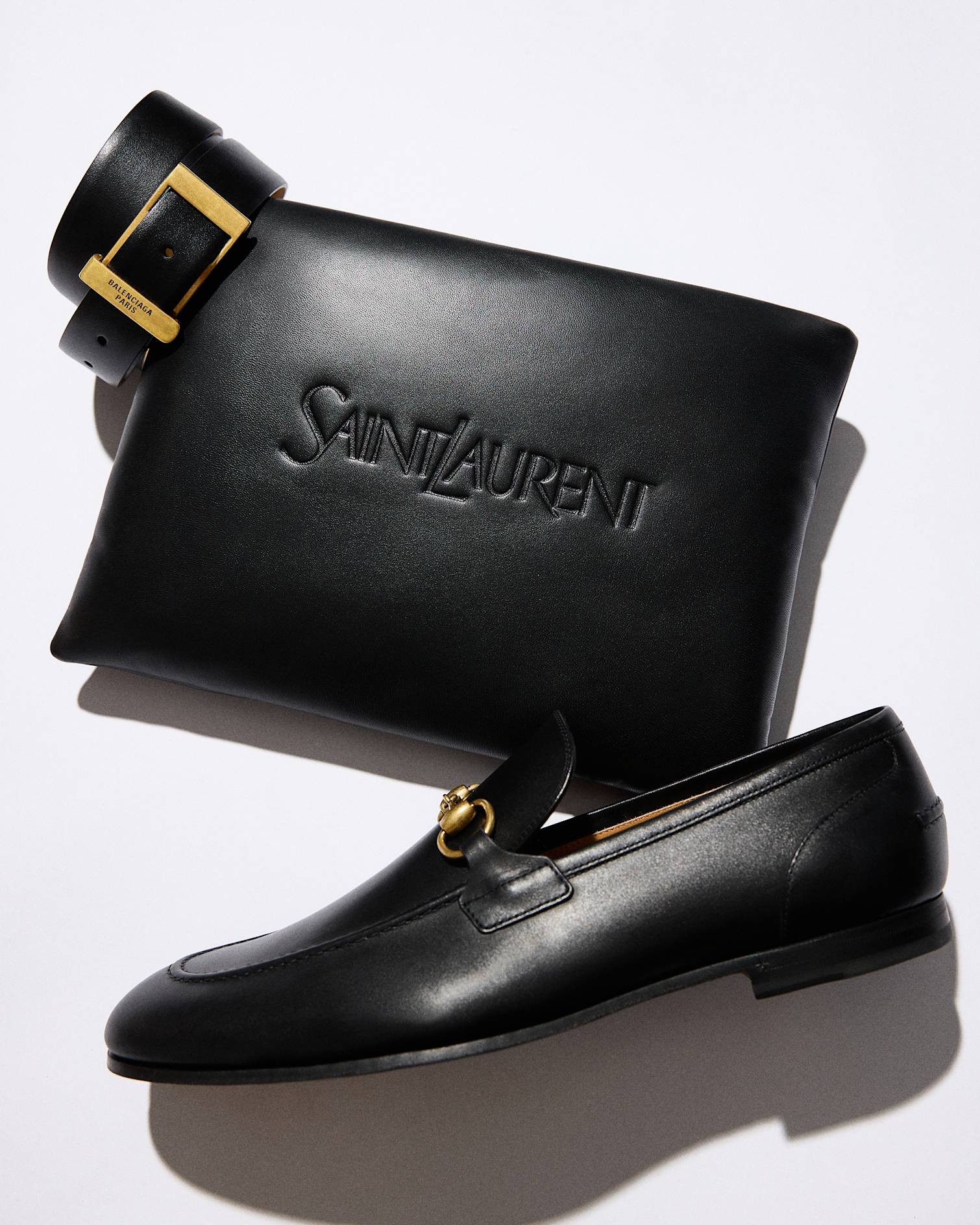 black leather belt with gold buckle, black leather pouch embossed with Saint Laurent, black leather Gucci loafer