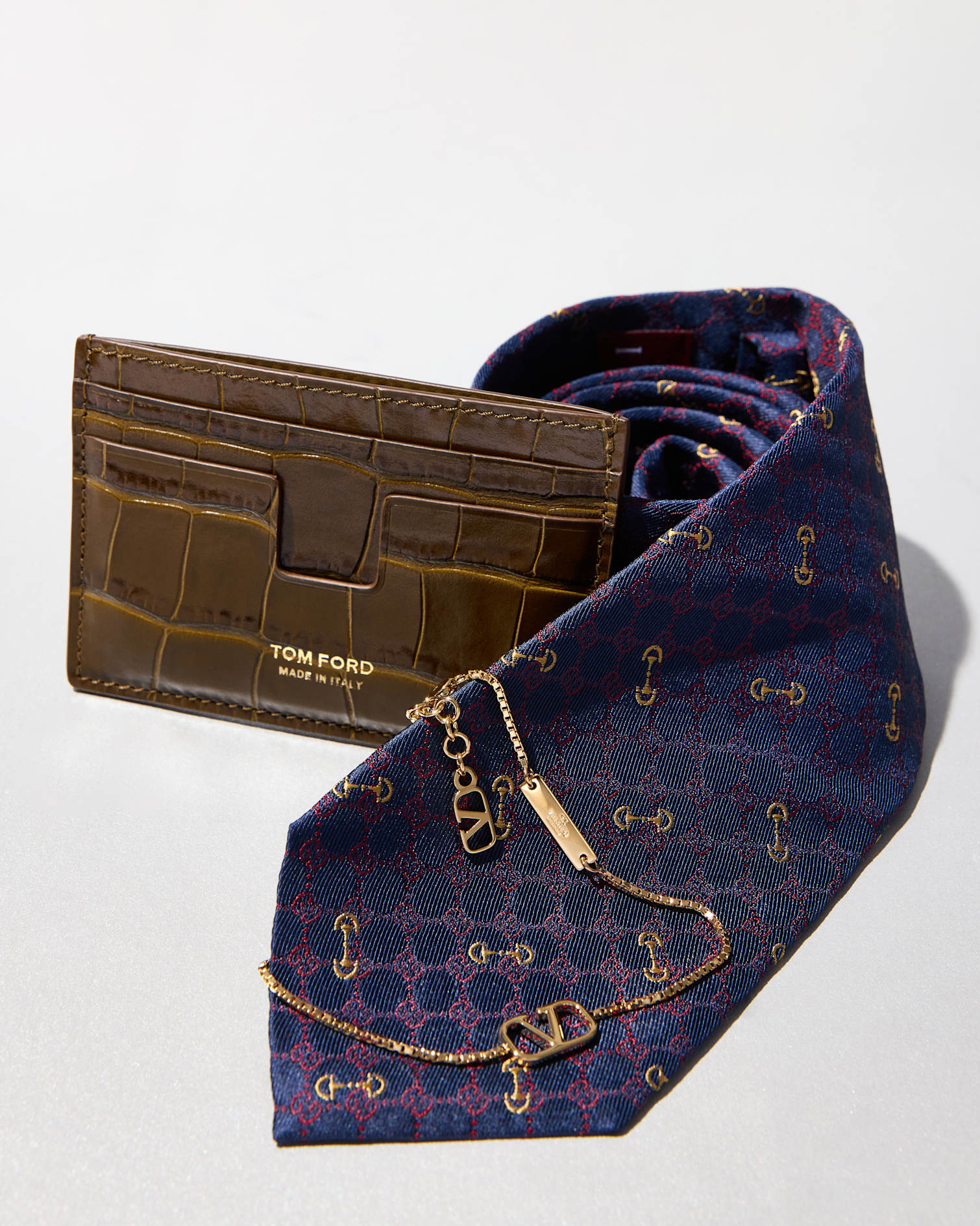 Tom Ford brown leather card holder next to Gucci dress tie and Valentino gold jewelry.