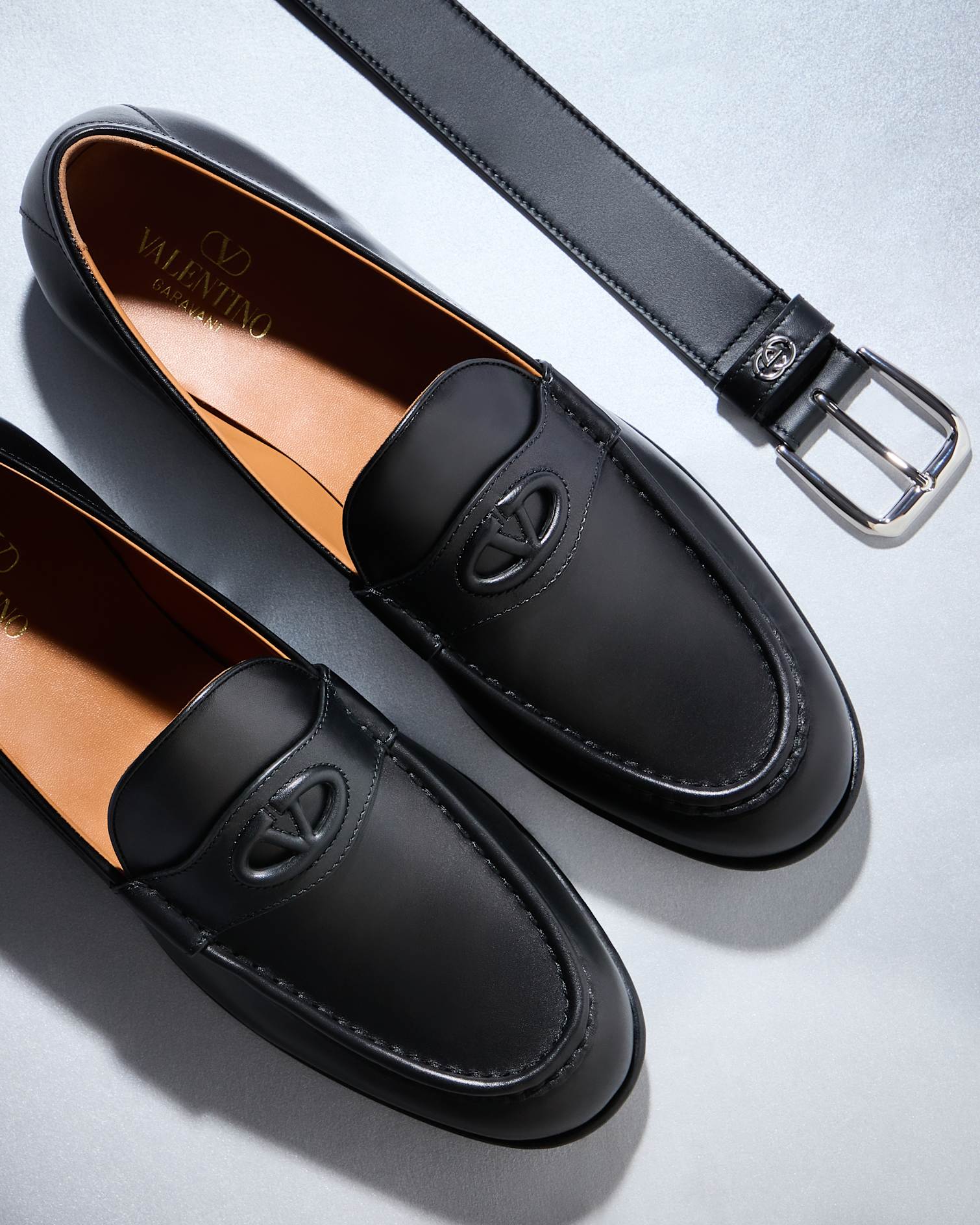 Black Valentino loafers are next to a black Gucci belt with a silver buckle.