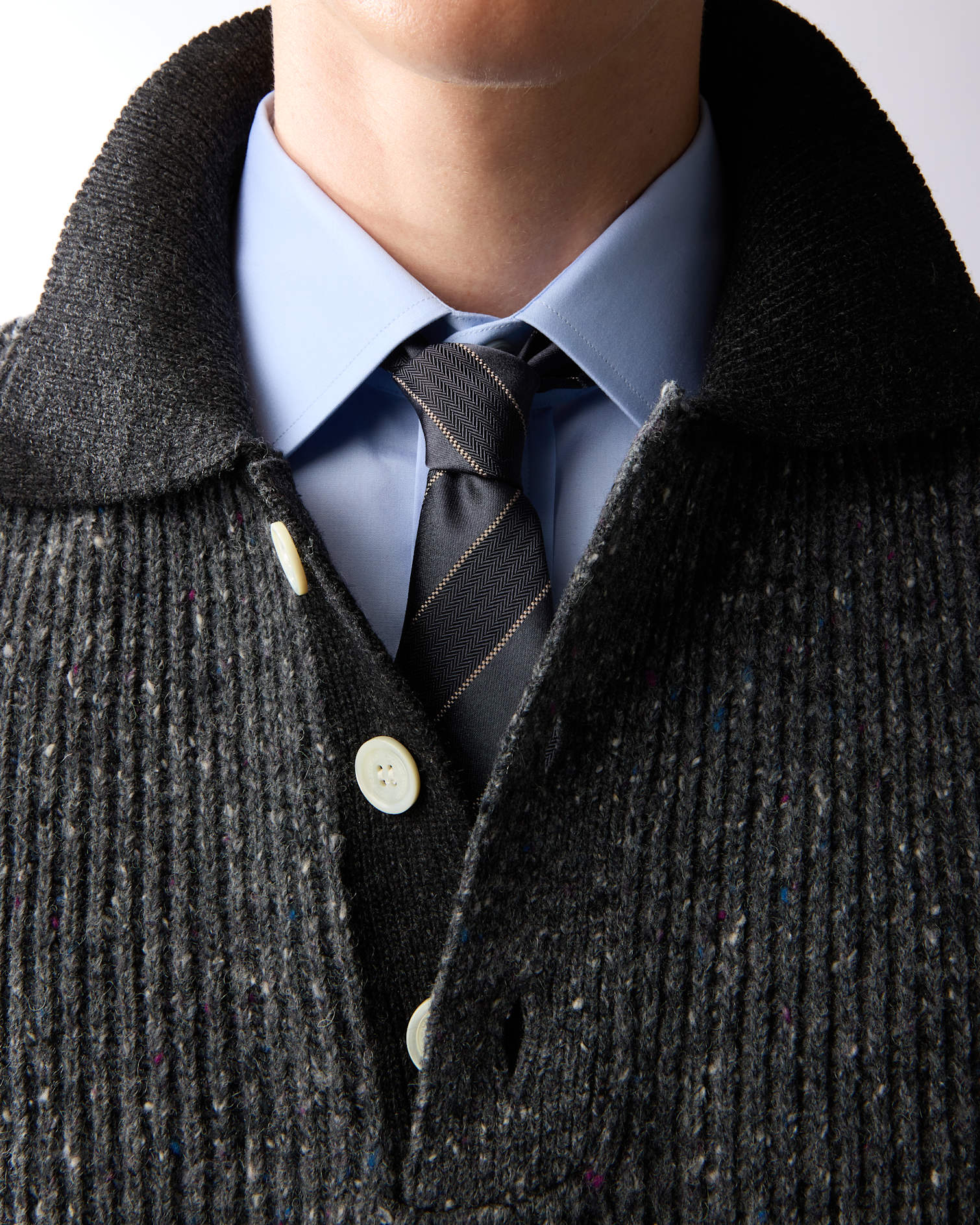 Detalle de un outfit como idea de regalo de Navidad para hombre: camisa azul, corbata de rayas y cárdigan de lana