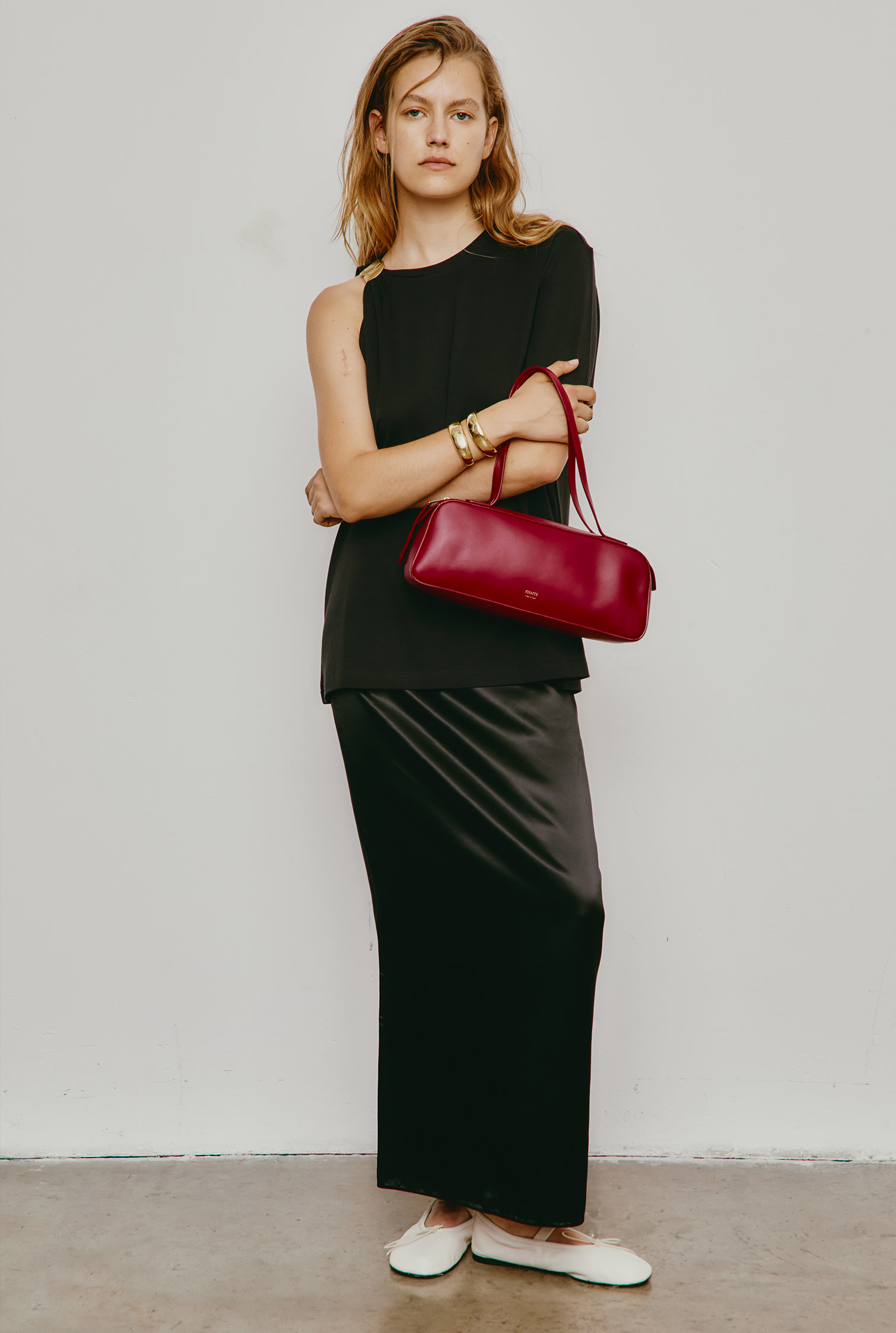 Model poses in black top and maxi skirt with Proenza Schouler white leather Mary Jane flats and burgundy Khaite shoulder bag