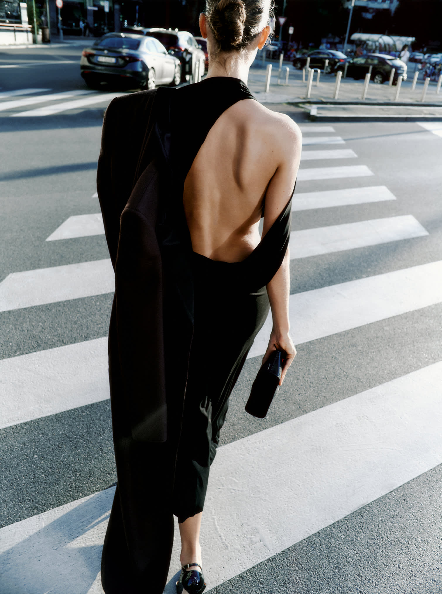 Das Model trägt das Midikleid „La Robe Salerno“ von Jacquemus, einen langen Mantel aus Viskosemischung in Dunkelbraun von Khaite Bellow und die Clutch „The Row Mel“.