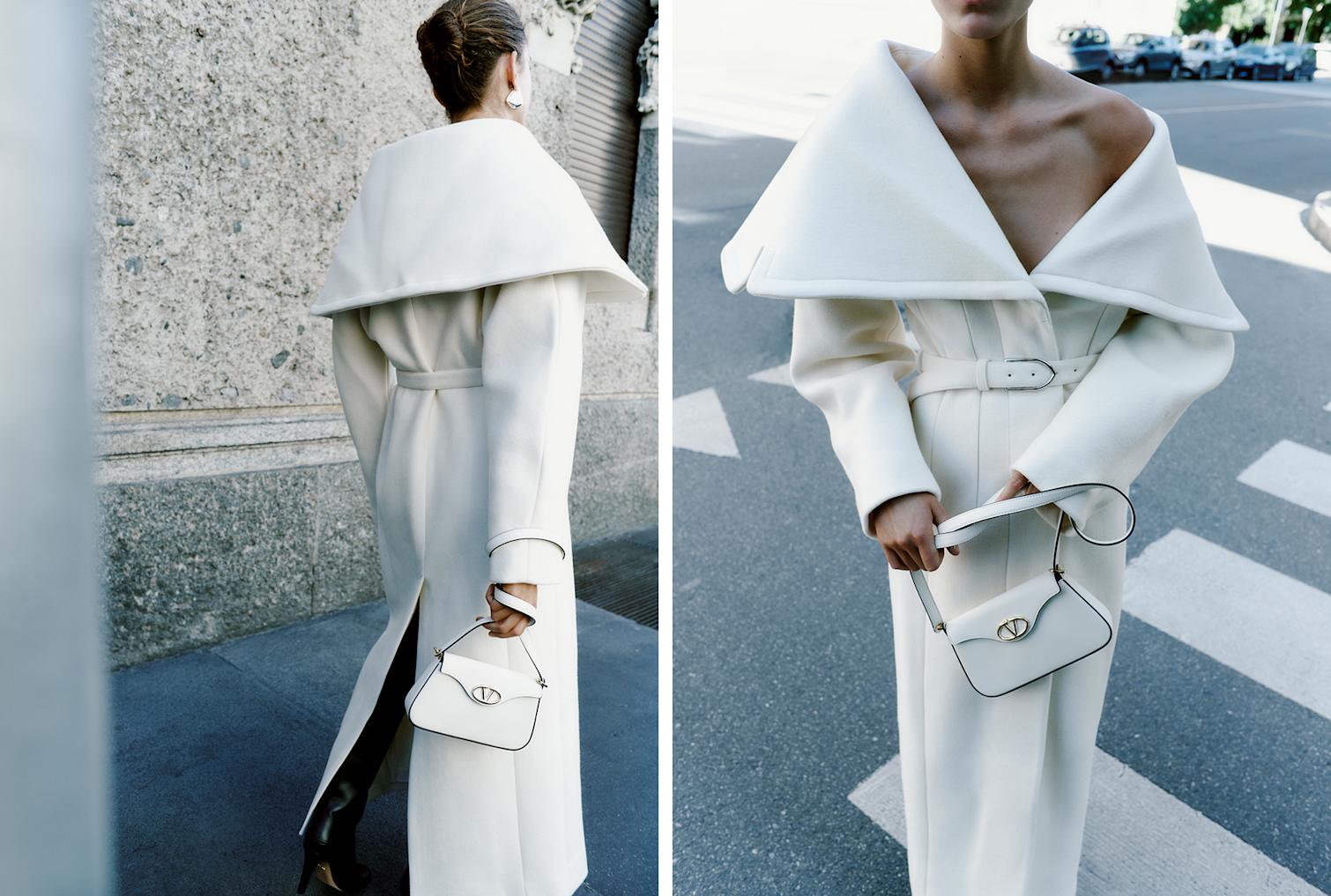 Das Model trägt einen langen Wollmantel von Jacquemus Le Manteau Caruso in Weiß und eine weiße Umhängetasche Mini Vlogo Bold von Valentino Garavani.