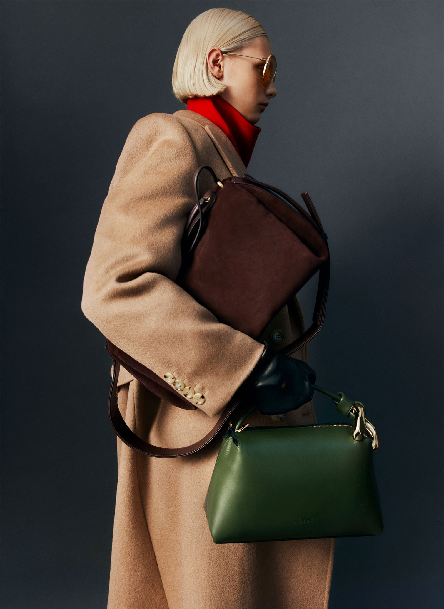 Cappotto lungo color cammello, maglia a collo alto rossa, borsa in pelle verde e borsa bauletto in camoscio marrone