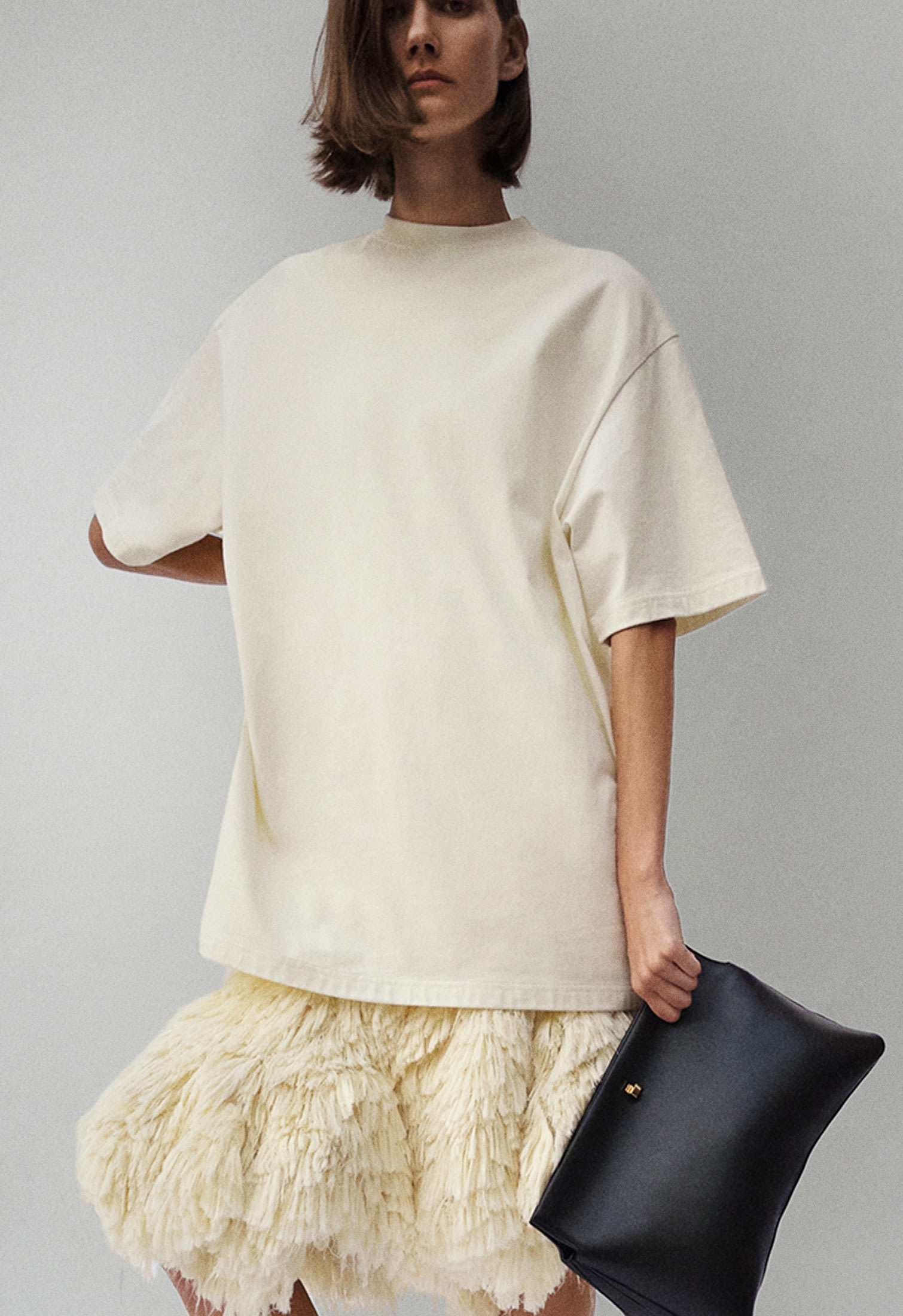 woman wearing an oversized off-white t-shirt, fluffy skirt and black clutch