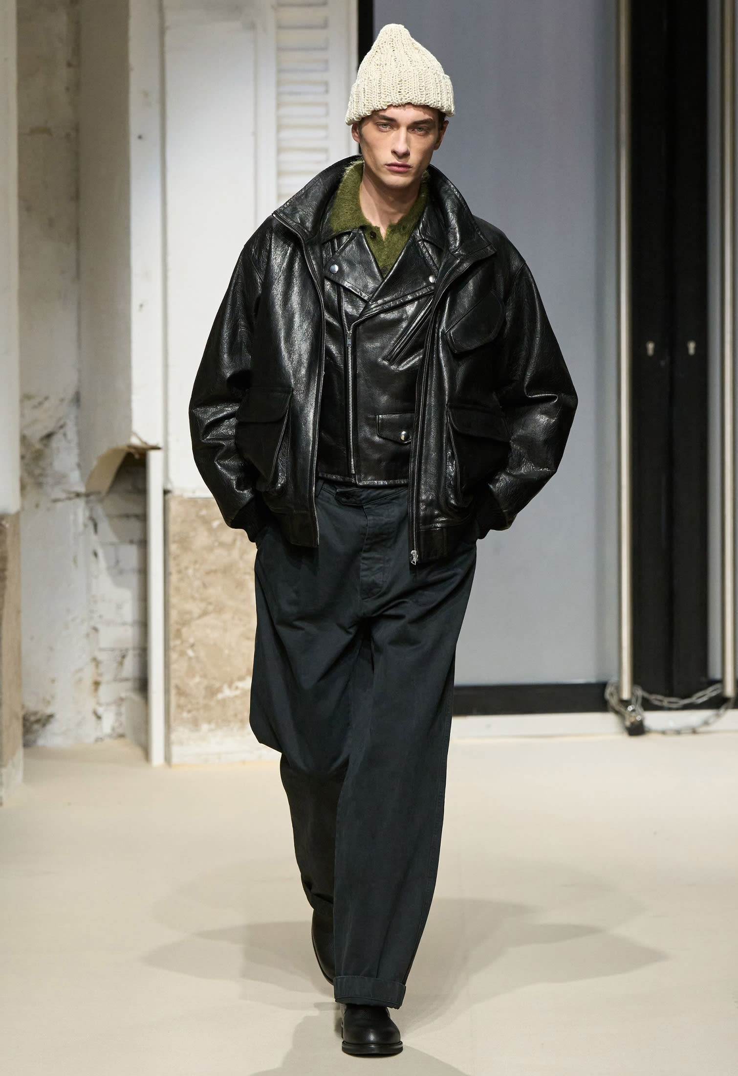 Look from Auralee runway with layered leather jackets, knit beanie hat and oversized black twill pants