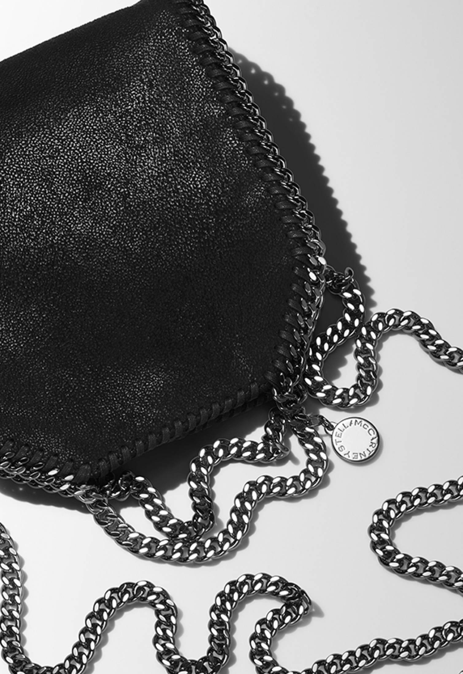 Woman wearing a beige suit and holding a black Stella McCartney bag with gold chain detail