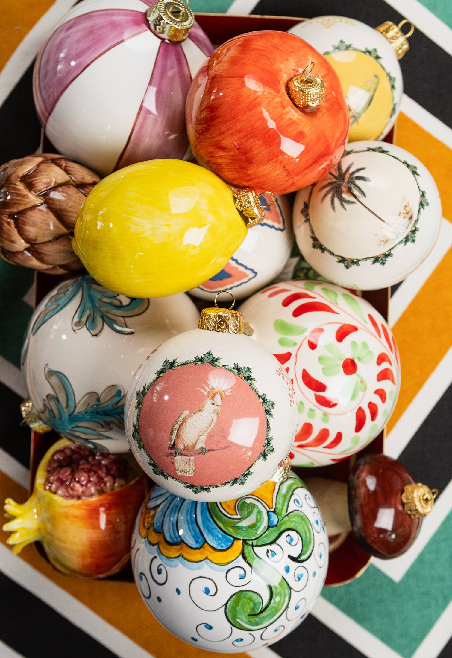 Assorted hand-painted ceramic Christmas decorations by Les Ottomans, featuring fruit and floral motifs in vibrant colors.